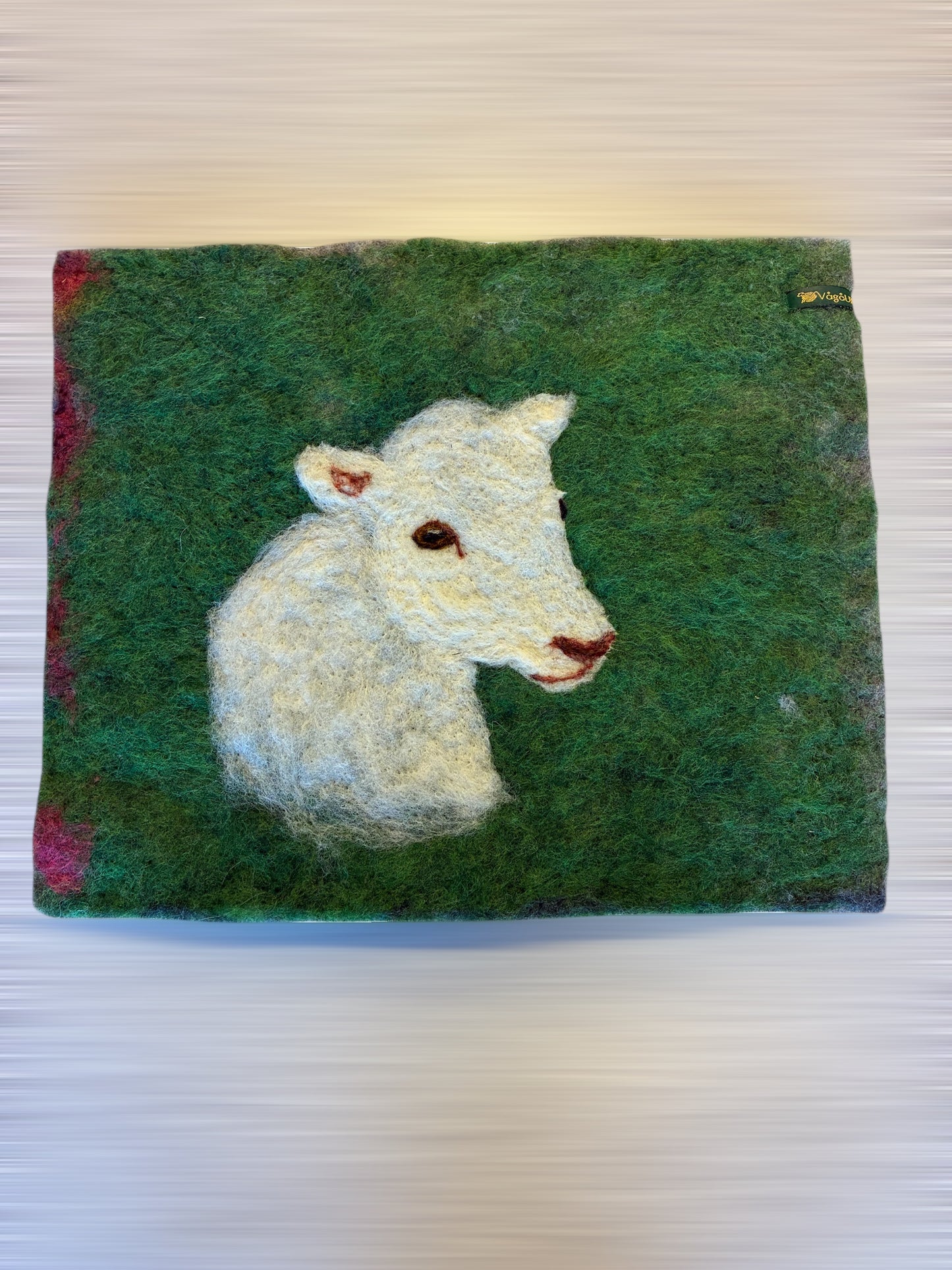 Sitteunderlag med nålefilta sauehodet og håndfarga ull som bakgrunn