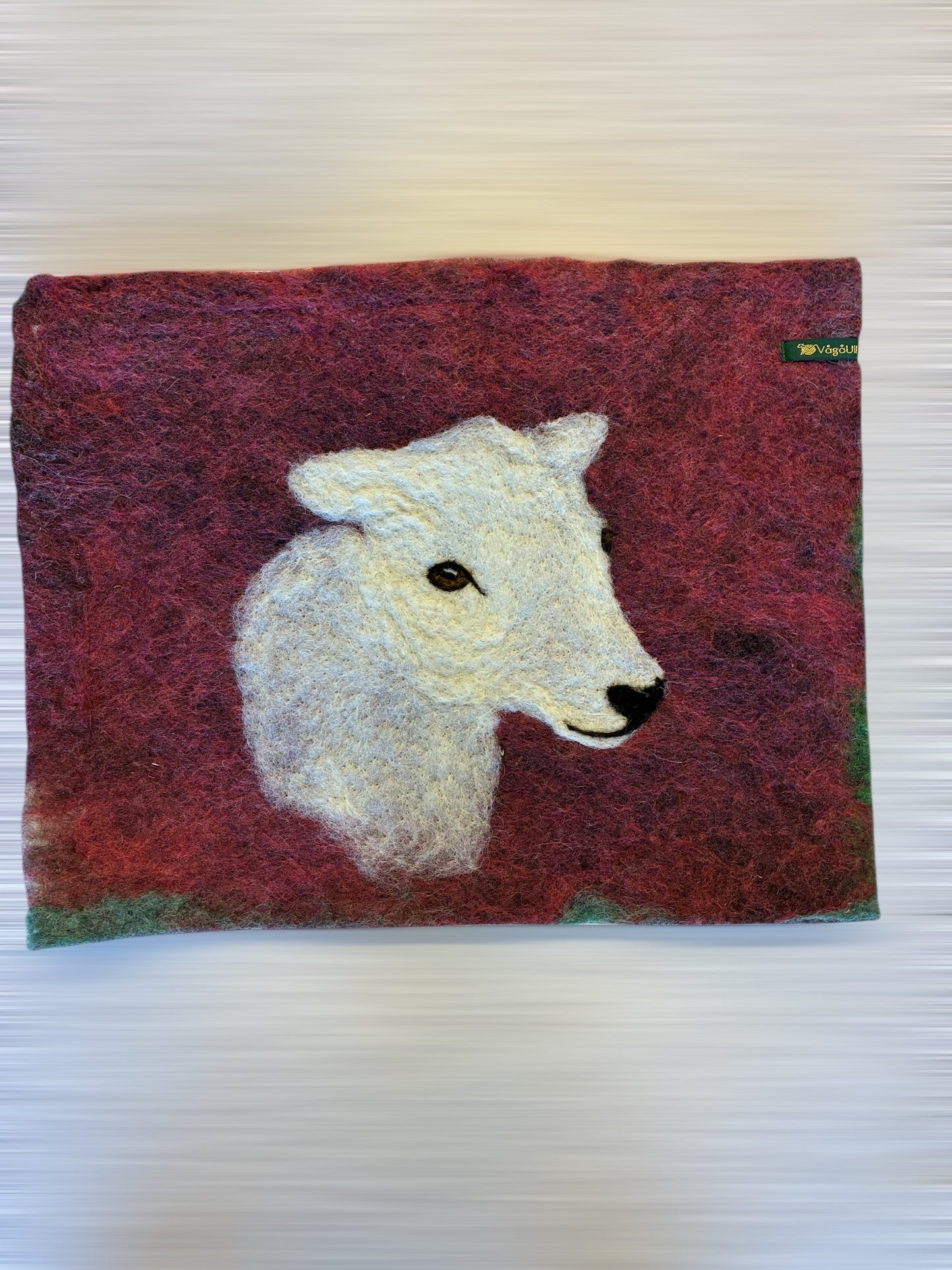 Sitteunderlag med nålefilta sauehodet og håndfarga ull som bakgrunn