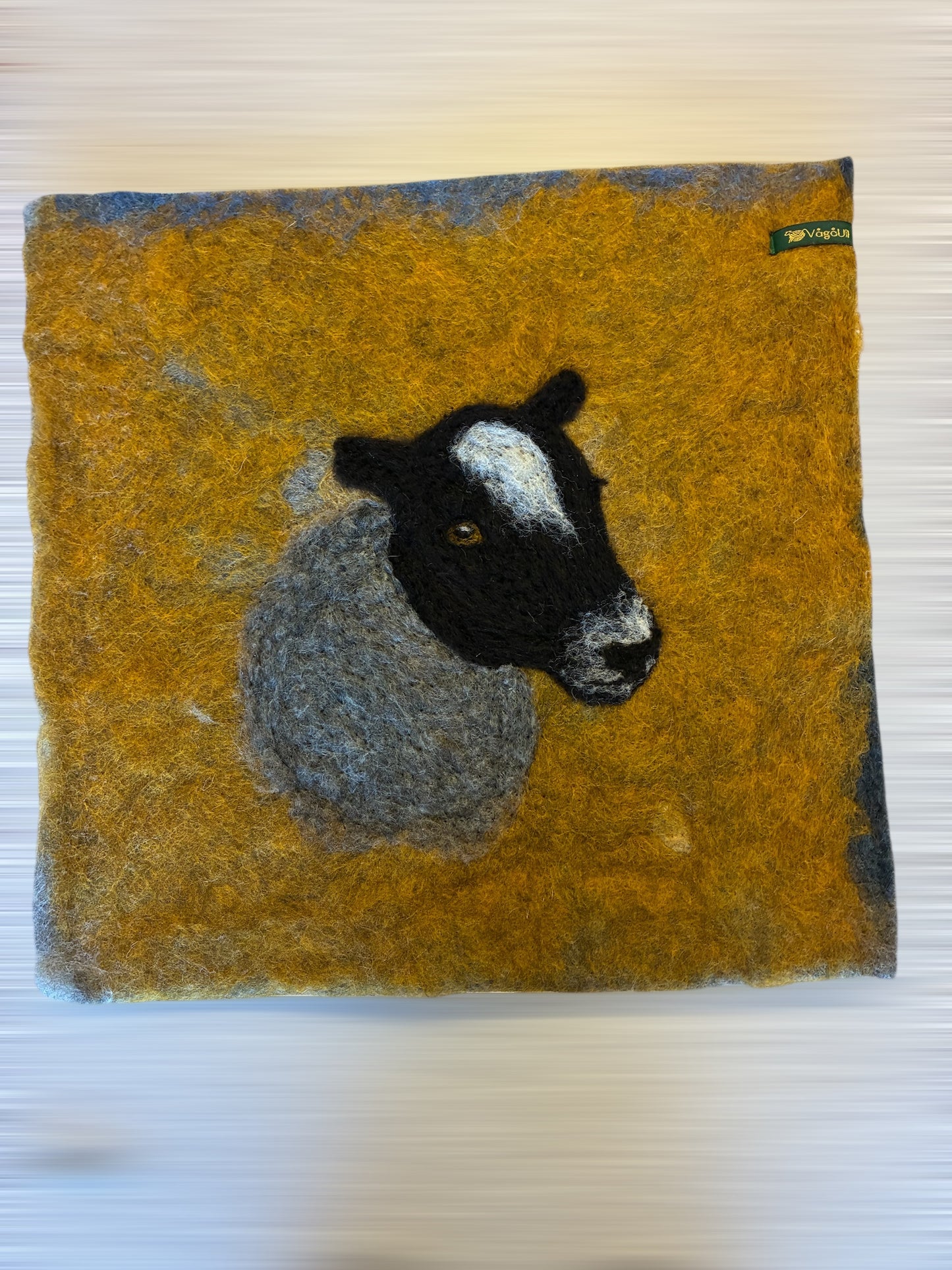 Sitteunderlag med nålefilta sauehodet og håndfarga ull som bakgrunn