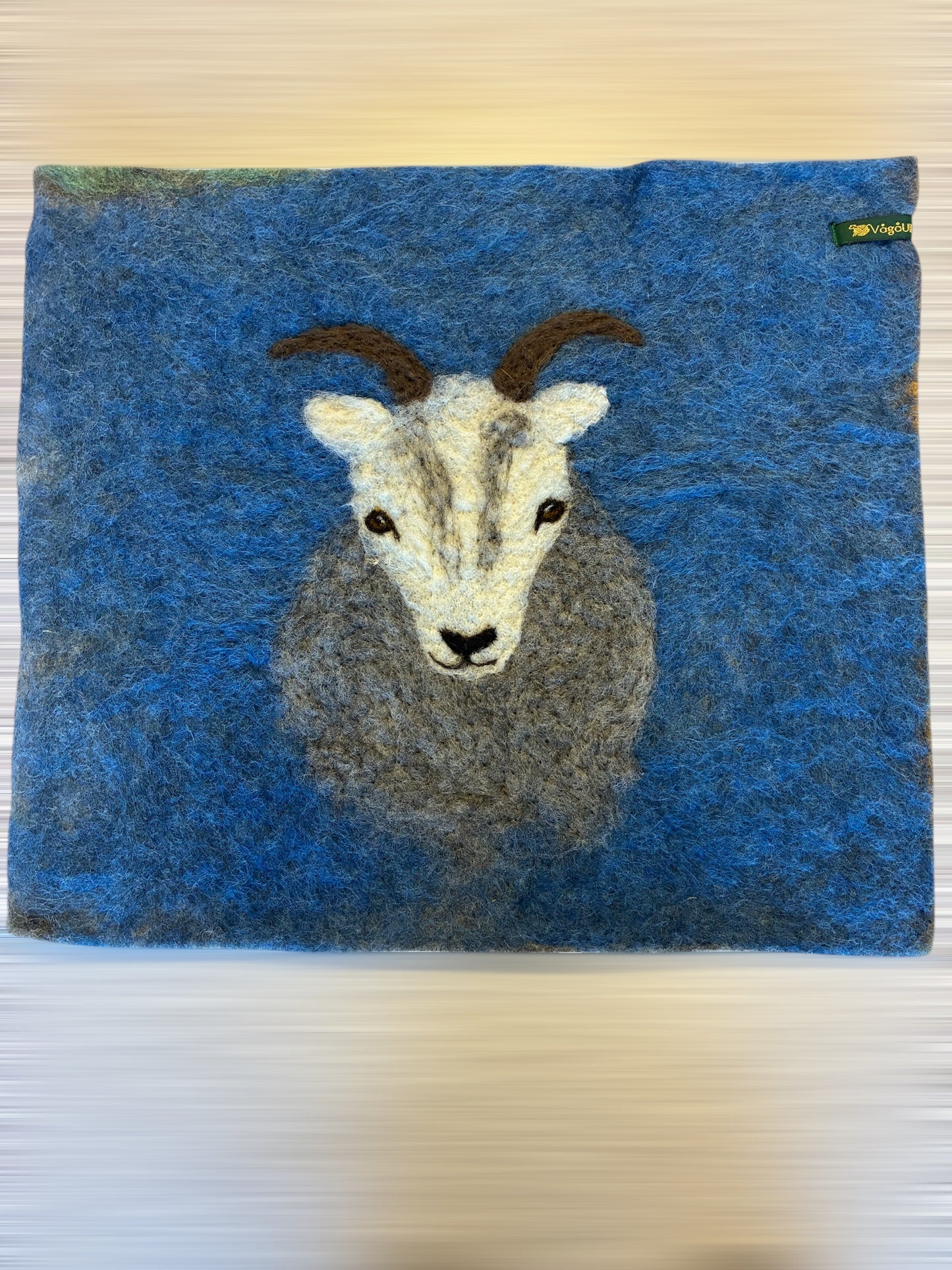 Sitteunderlag med nålefilta sauehodet og håndfarga ull som bakgrunn
