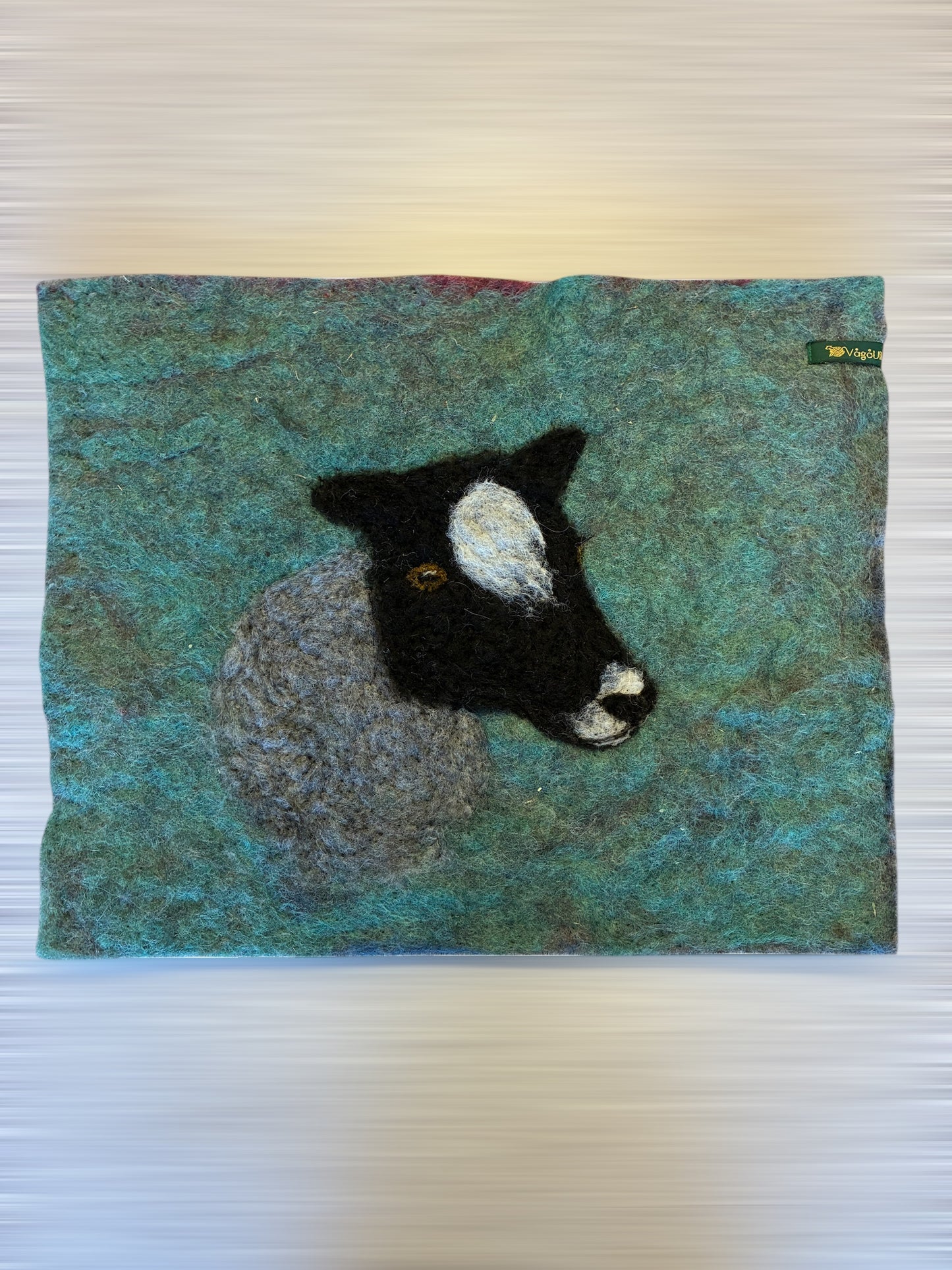 Sitteunderlag med nålefilta sauehodet og håndfarga ull som bakgrunn